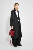 Model wearing Wayfair Black Trench Coat, stylish look with red handbag and casual outfit.