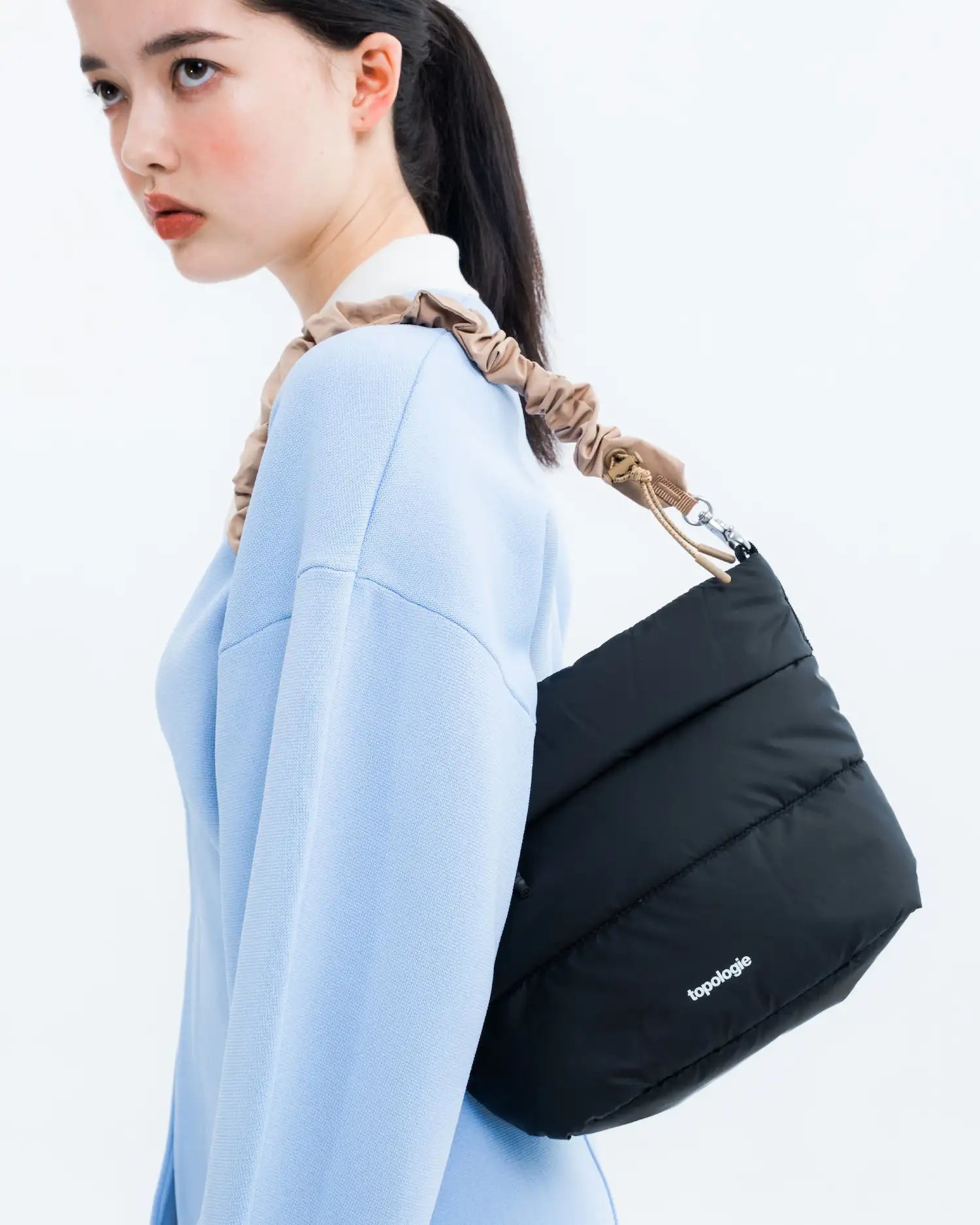 Woman wearing a Besace Ecru Matt Coated Bag with a stylish strap, showcasing its modern design and functionality.