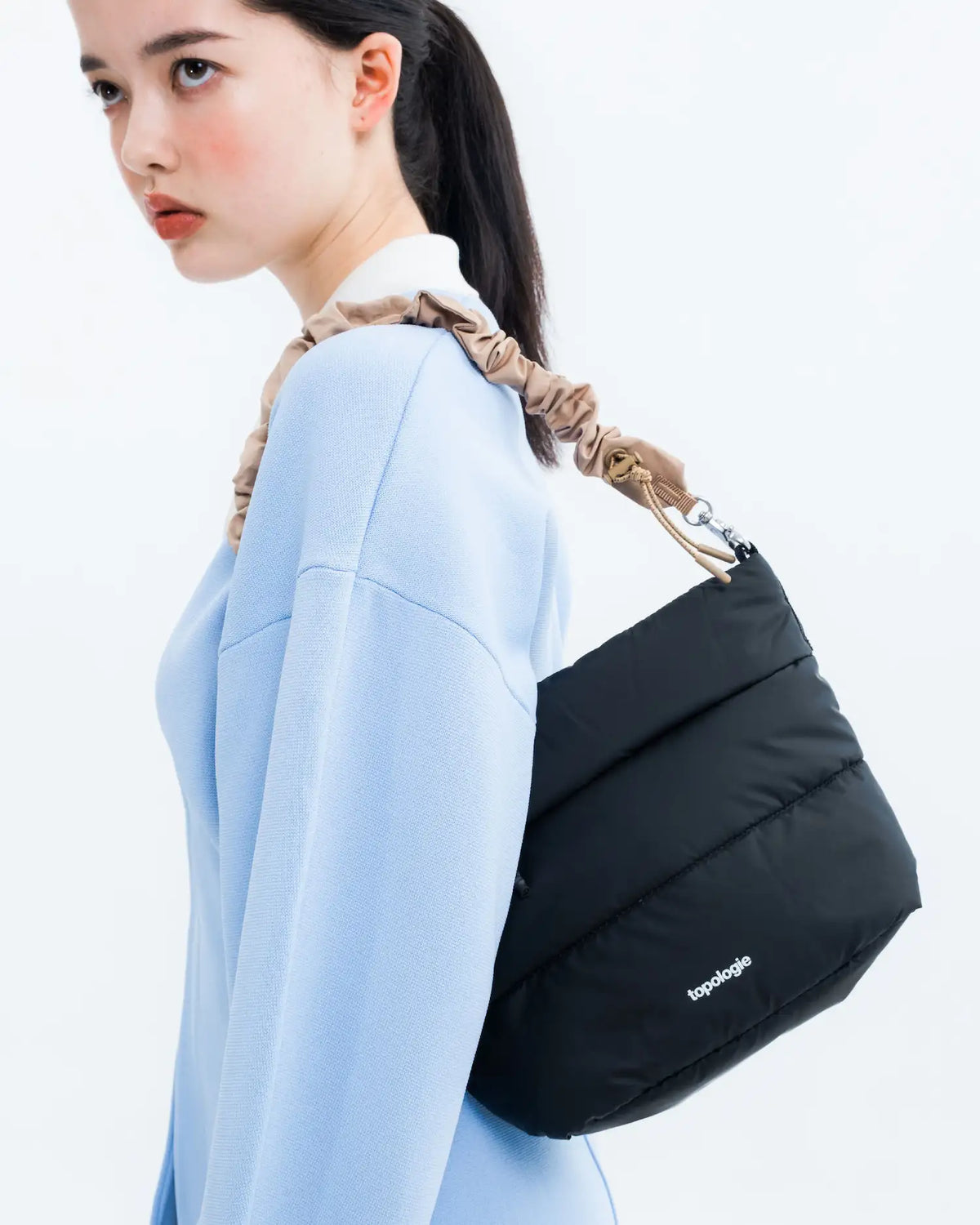 Besace Chambray Silky Peach Bag worn by a model with a light blue sweater, showcasing its stylish design.
