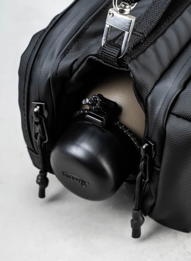 Bottle Sacoche Medium Ivy Green Papery Bag with a black water bottle securely fit inside its zipped compartment.