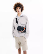 Model wearing a Bottle Sacoche Medium Ecru Matt Coated Bag with a stylish outfit on a white background.