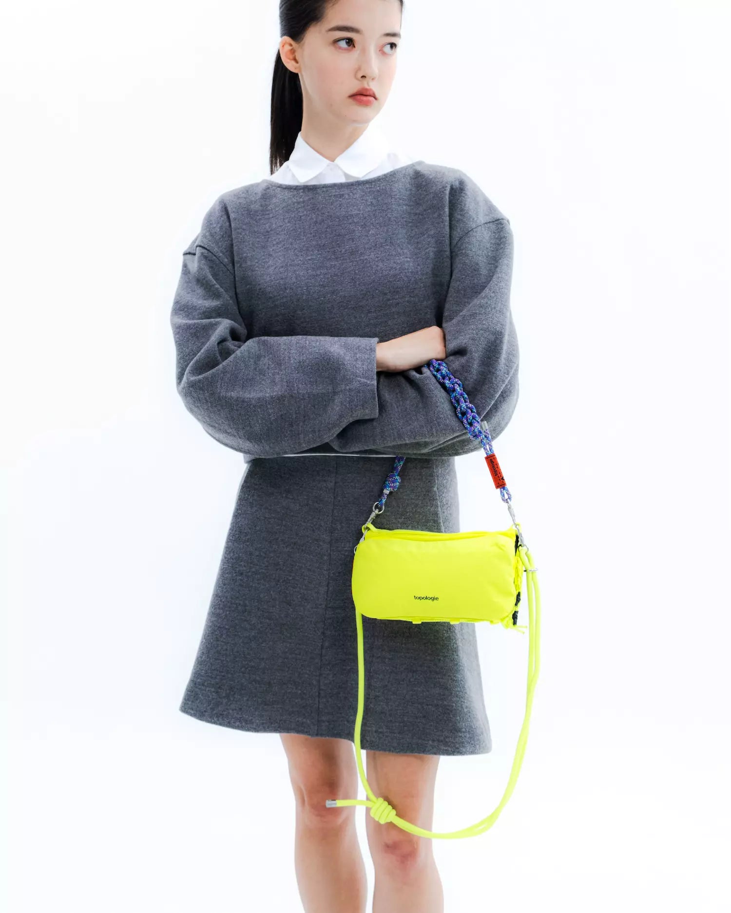 Model wearing Bottle Sacoche Medium Blue Check Wool Bag in bright yellow, styled with a gray outfit.
