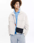 Man wearing Phone Sacoche 90 Purple Washed Silk Nylon Bag, stylish outfit with a light jacket and blue polo.