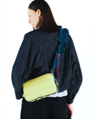 Model wearing the Bottle Sacoche Large Moss Silky Peach Bag in a vibrant yellow color with an elegant strap.