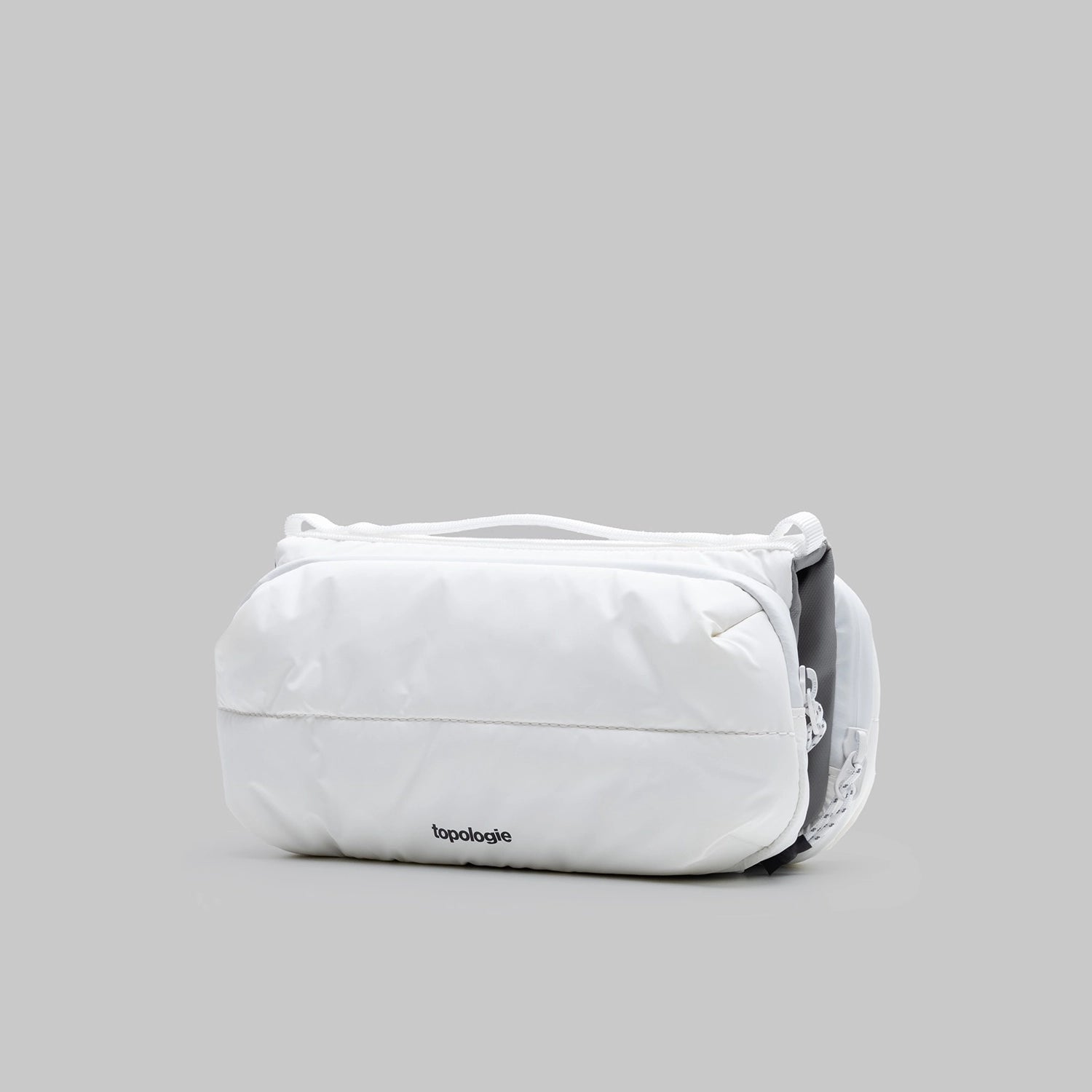 Bottle Sacoche Medium Ecru Matt Coated Bag on a gray background showcasing its water-repellent fabric and sleek design.