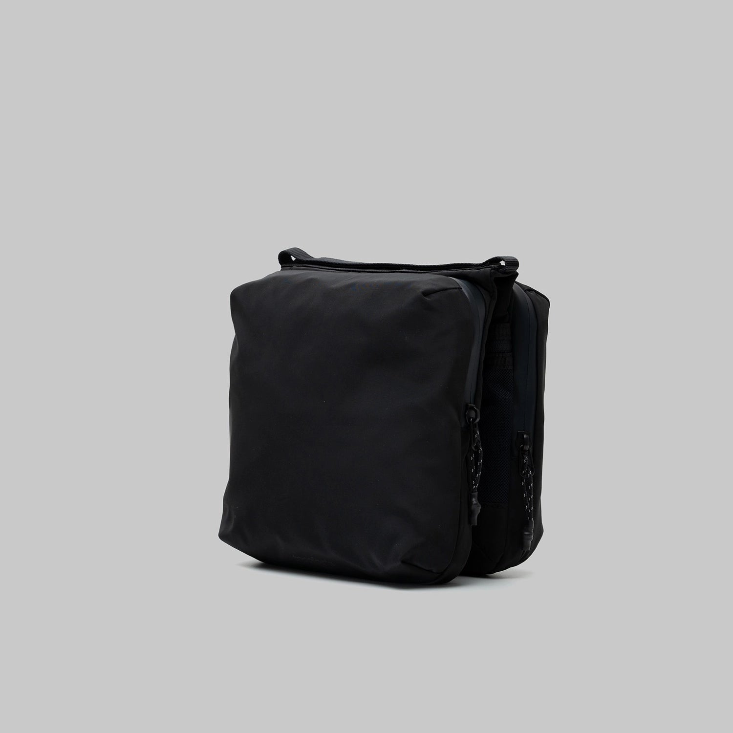 Cassette Sacoche Medium Black Tech Sateen Bag from the side view, showcasing sleek design and zippered compartments.