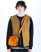 Cassette Sacoche Medium Moss Tech Sateen Bag worn by a model with an orange bag and beige vest.