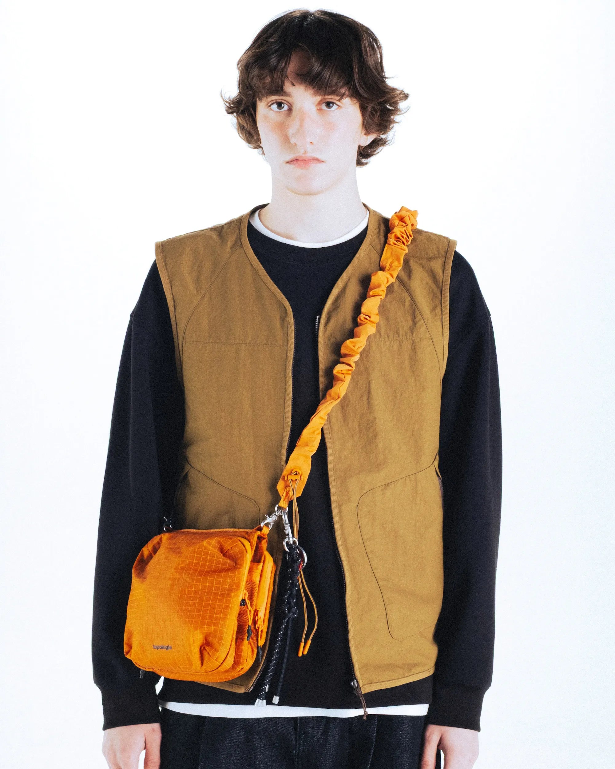 Cassette Sacoche Medium Moss Tech Sateen Bag worn by a model with an orange bag and beige vest.