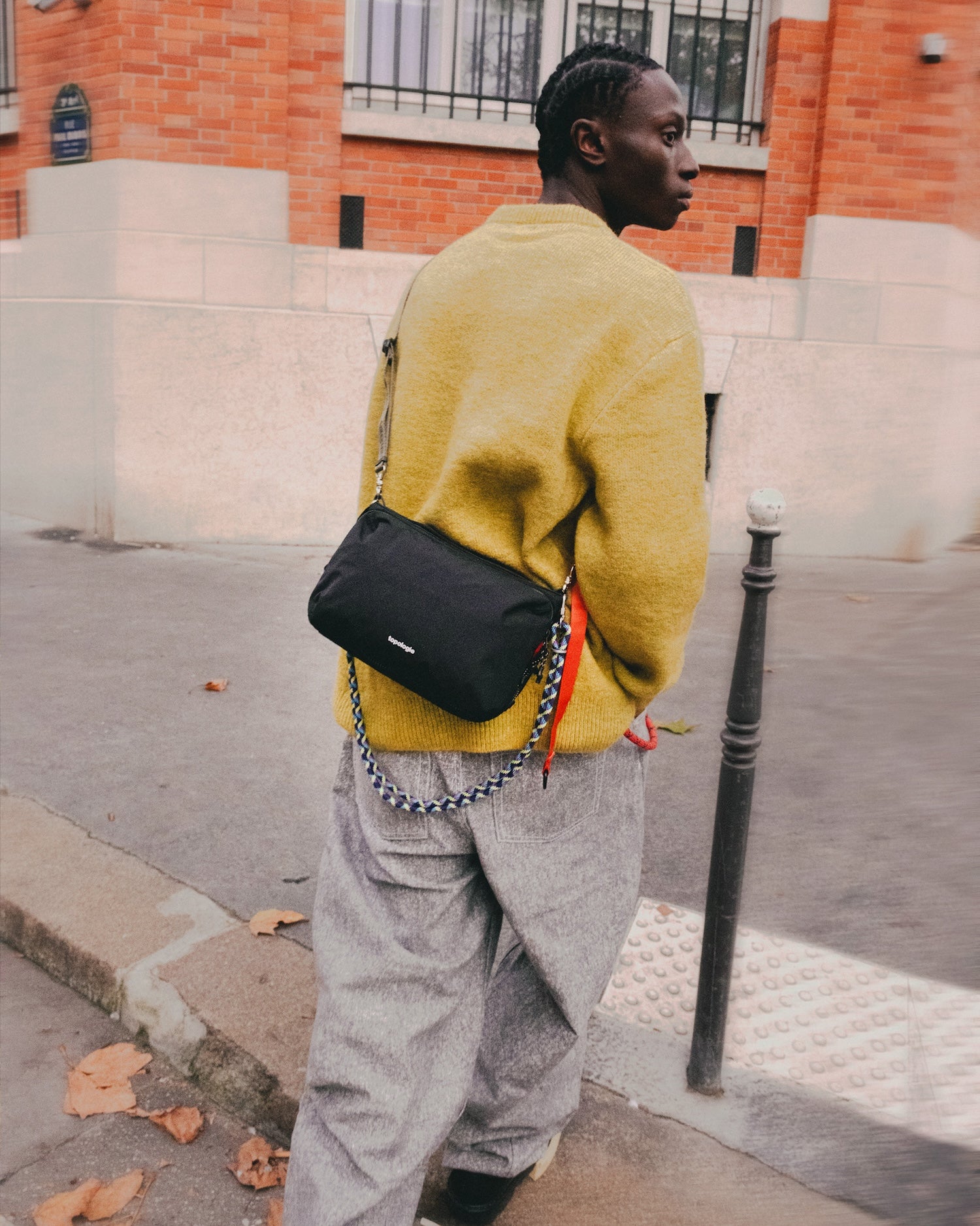 A person wearing a yellow sweater and gray pants, showcasing a Bottle Sacoche Large Blue Check Wool Bag in an urban setting.