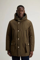 Arctic Parka Dark Green Coat displayed on a model, featuring a protective hood and patch pockets.