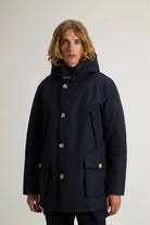 Man wearing Arctic Parka Melton Blue Coat with hood and patch pockets, styled for winter weather.