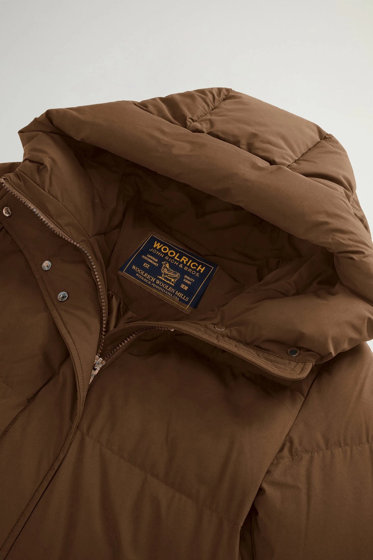 Madison Long Coat Dark Earth Coat featuring Woolrich branding and premium down filling for warmth.