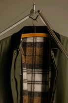 Waxed Coat Waxed Dark Green Coat hanging on a rack showcasing its plaid inner lining and velvet collar.